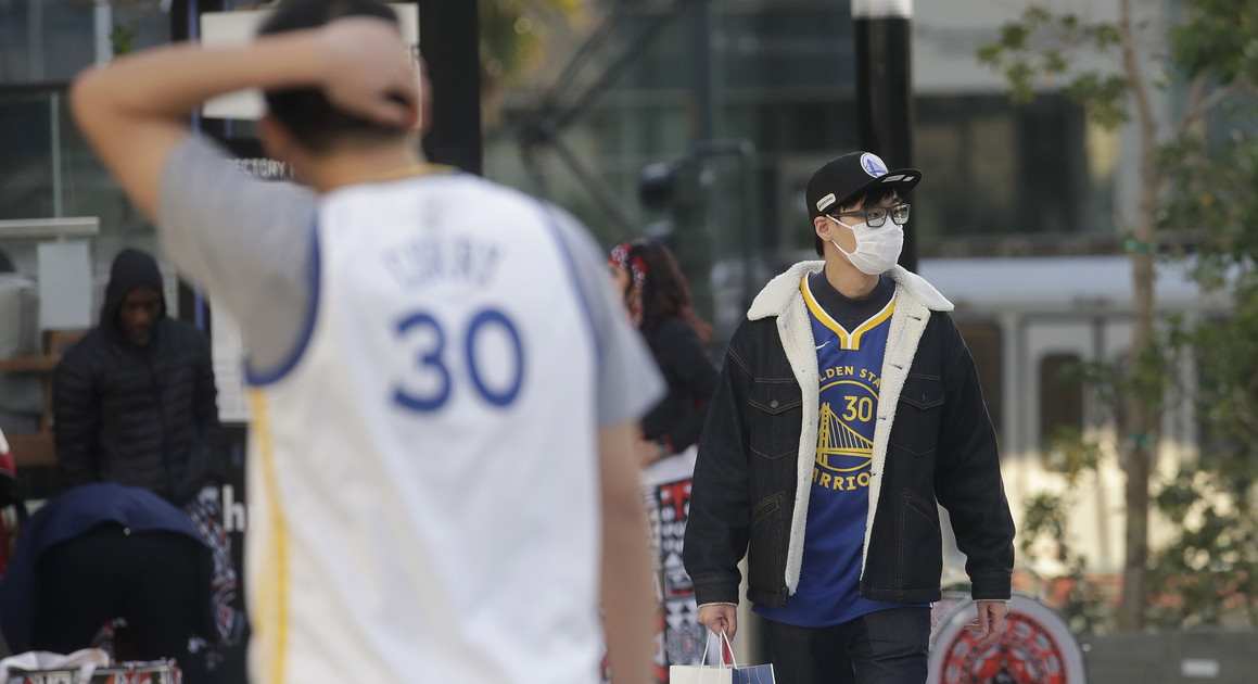 Golden State Warriors fan wears a mask because of the coronavirus outbreak outside of the Chase Center before attending an NBA basketball game | AP Photo