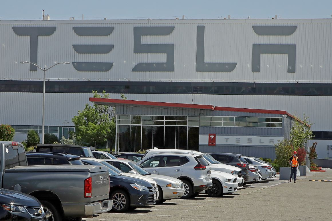 A masked man walks in the Fremont, Calif. Tesla plant parking lot on Monday. | AP Photo